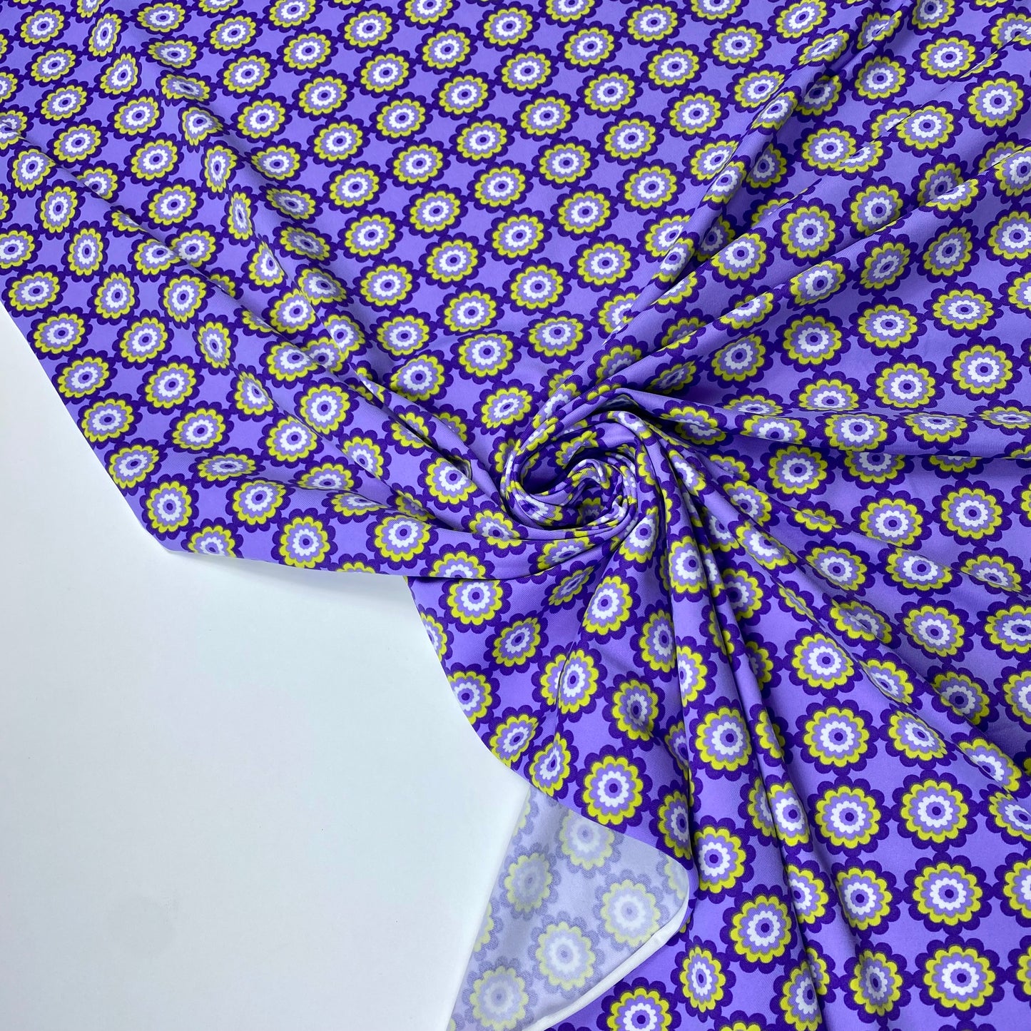 Tejido de punto lycra con fondo morado y flores verdes y lilas.