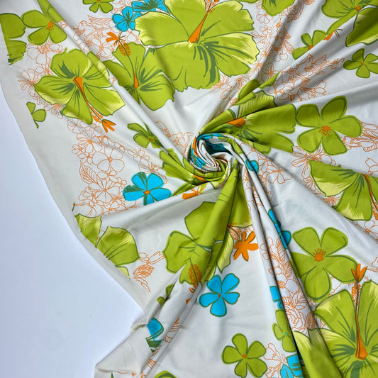 Tejido de punto de lycra de color blanco con grandes flores verdes y pequeñas flores azules.