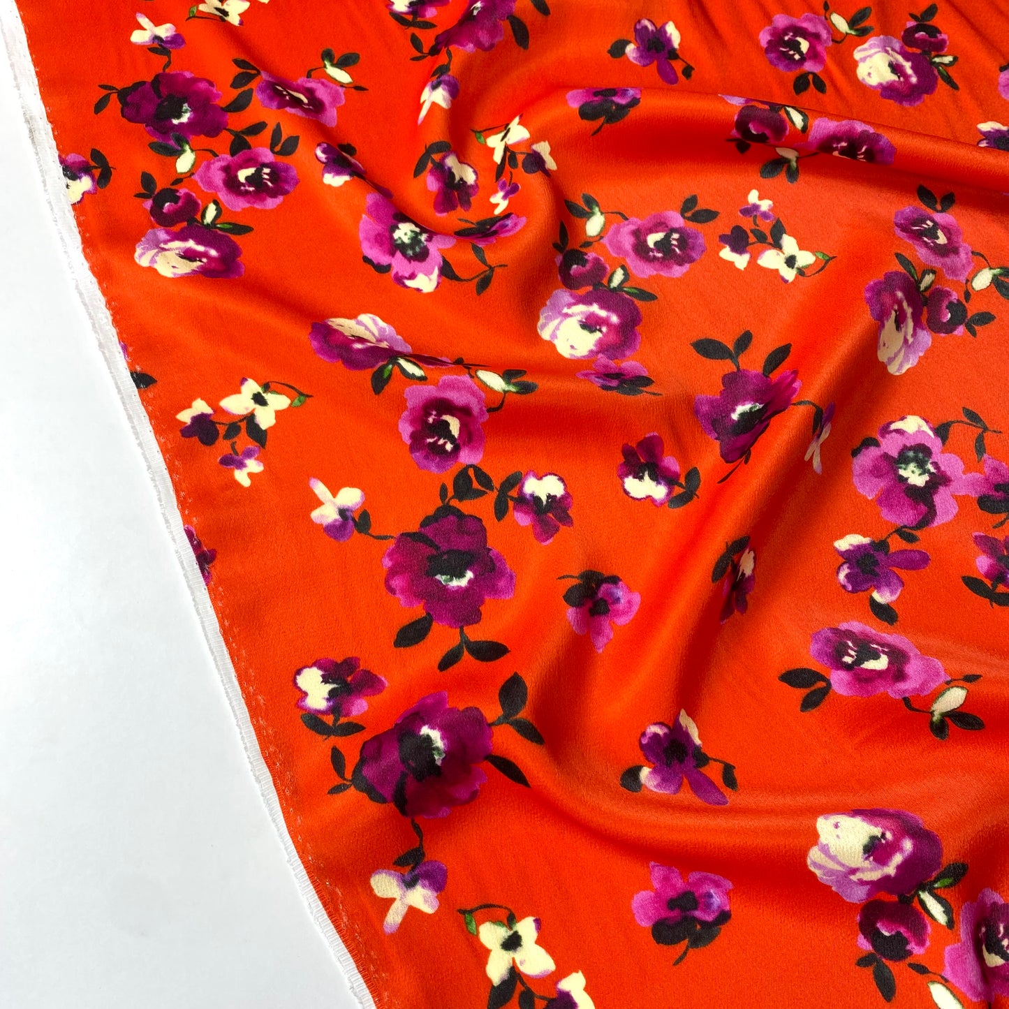 Tejido satinado con fondo naranja rojizo y flores violetas.