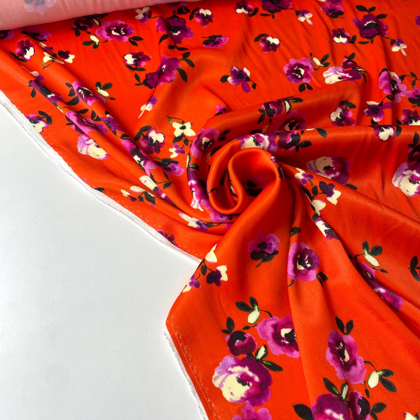 Tejido satinado con fondo naranja rojizo y flores violetas.